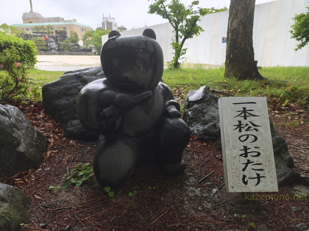 巻物を持つ一本松のおたけのたぬき像