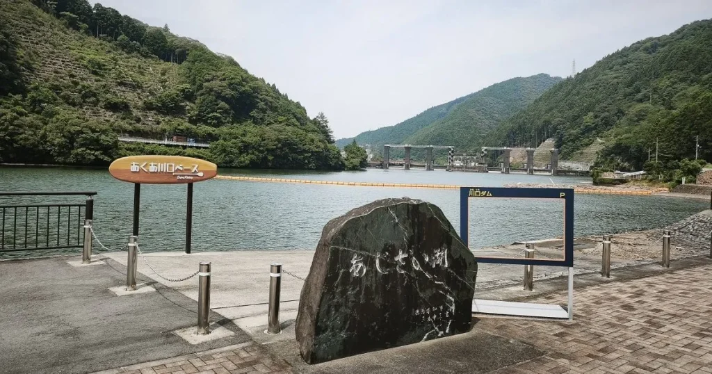 あくあ川口ベースの看板とあじさい湖の石碑、川口ダムを望むダムカード型フォトスポット