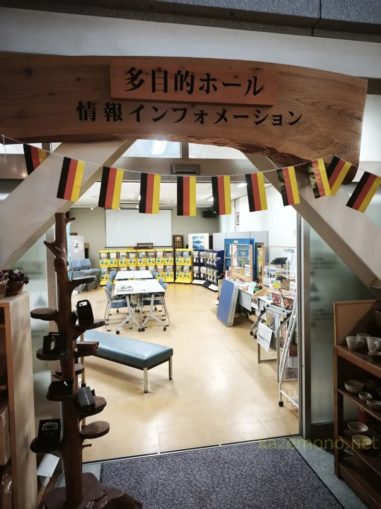 売店側から見た机と椅子や観光案内、ガチャガチャが並ぶ多目的ホール入口