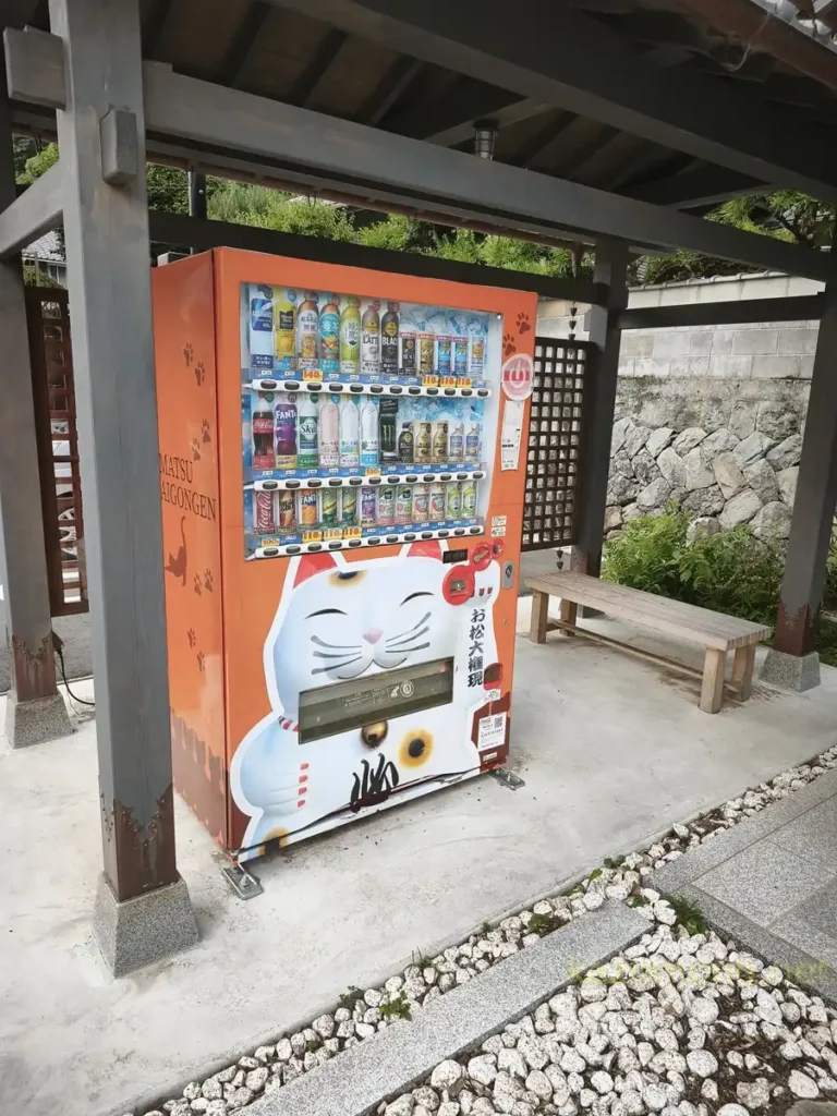 お松大権現仕様の猫が描かれた自販機と横のベンチ