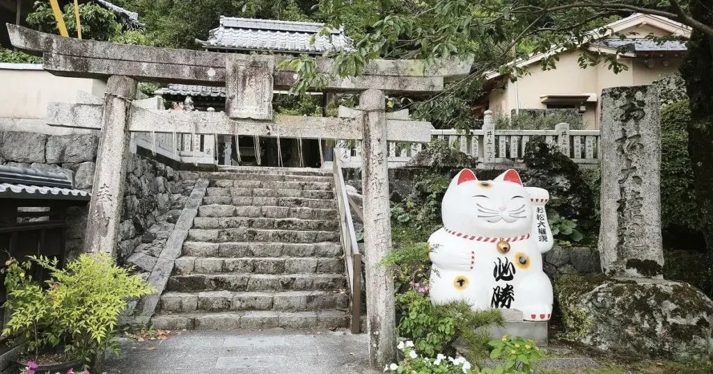 お松大権現の「必勝」と書かれた大きな招き猫と石柱